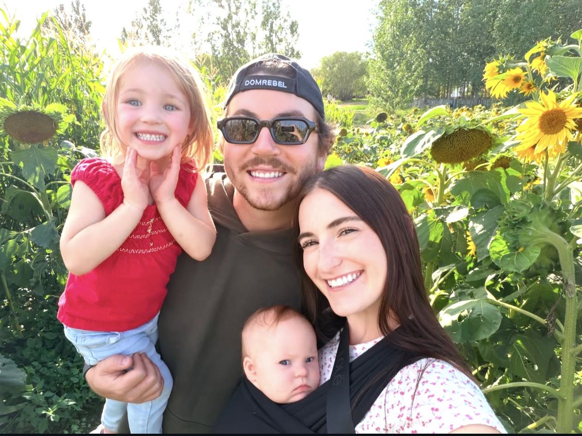 Aidan with his wife and their two kids in a sunflower field